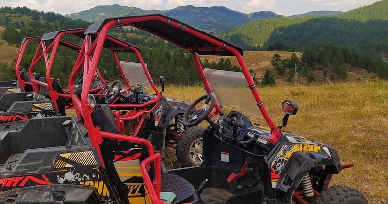 Side-by-side UTVs parked on grassy trail with mountain views