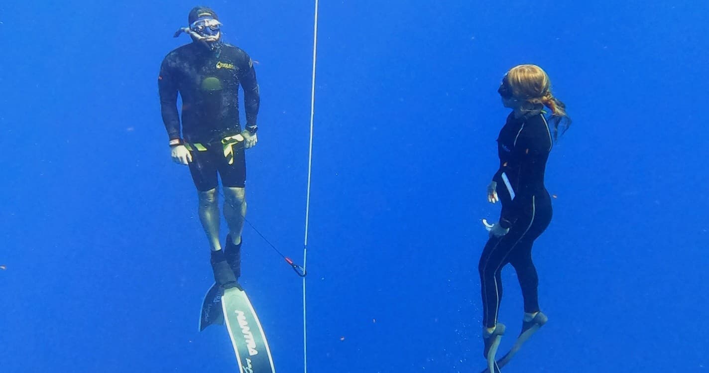 Freedivers training at descent line in deep blue open ocean