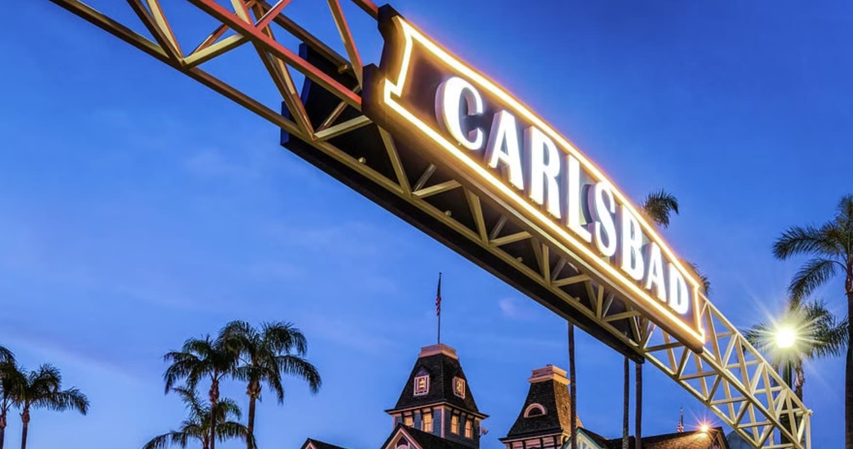Carlsbad entrance sign at dusk with palm trees and sky