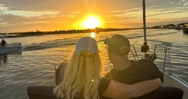 Couple watching sunset from sailboat on calm coastal water