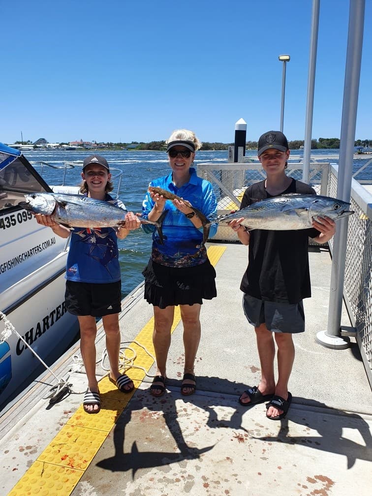 Three anglers holding tuna on marina dock under clear blue sky