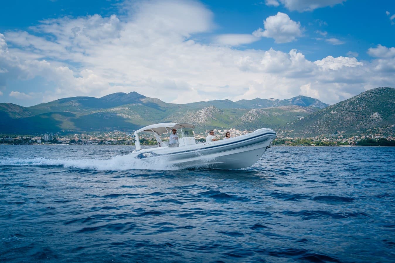 White motorboat cruising coastal waters with mountain backdrop