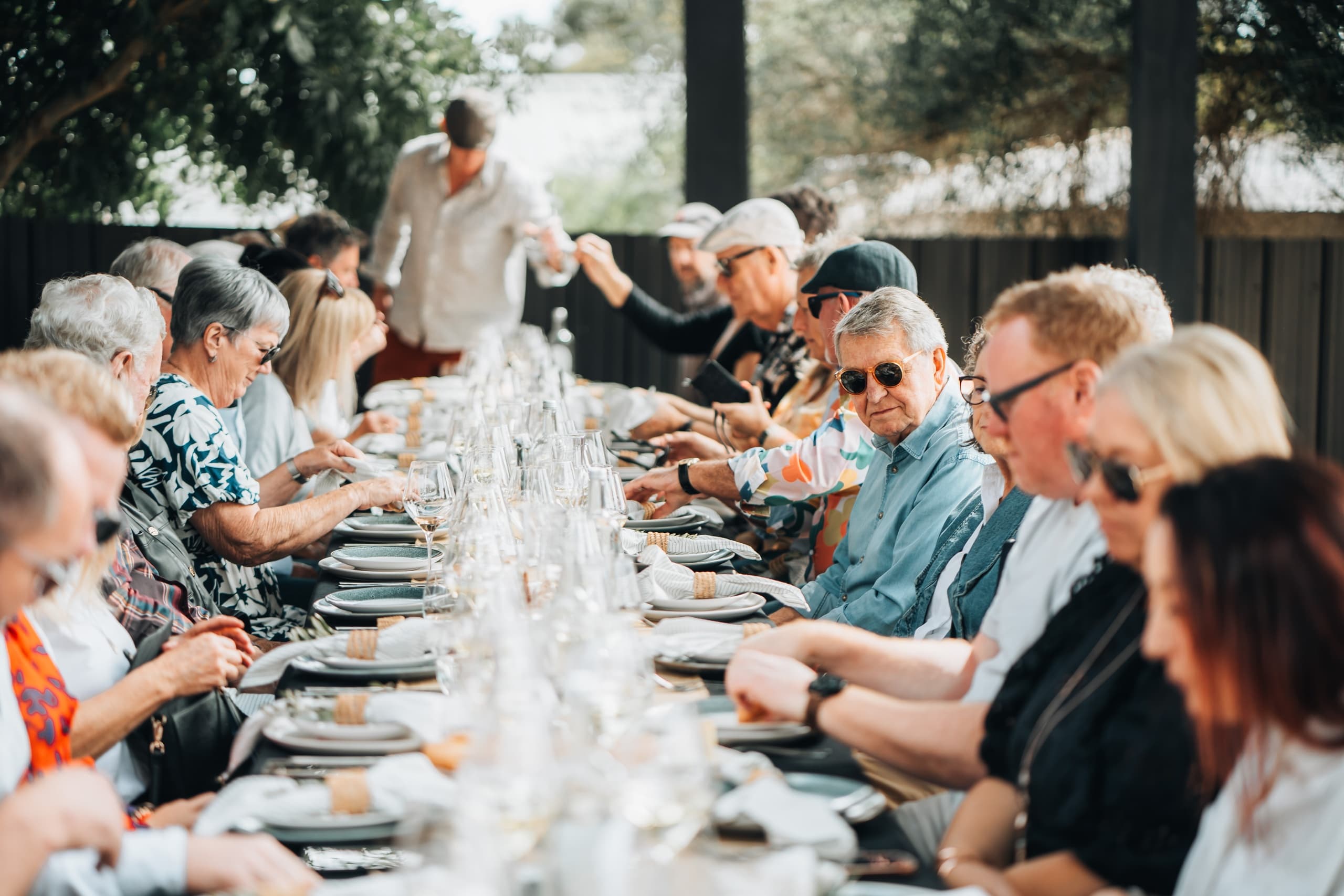 Long outdoor communal wine lunch under trees at winery