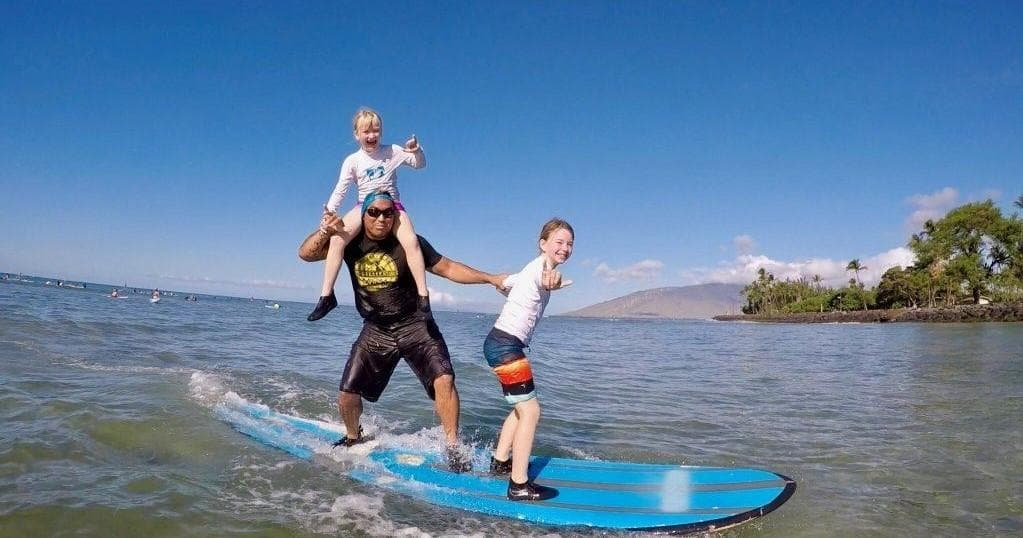 Instructor and kids balancing on surfboard in shallow Maui waters
