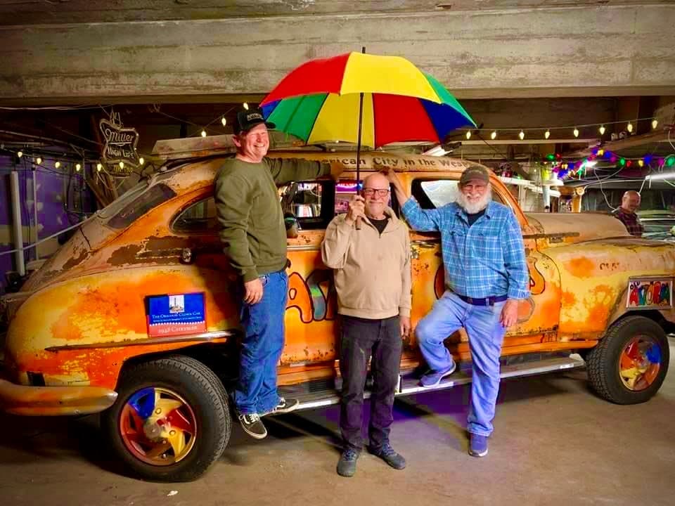 Three men posing with vintage painted car inside covered garage