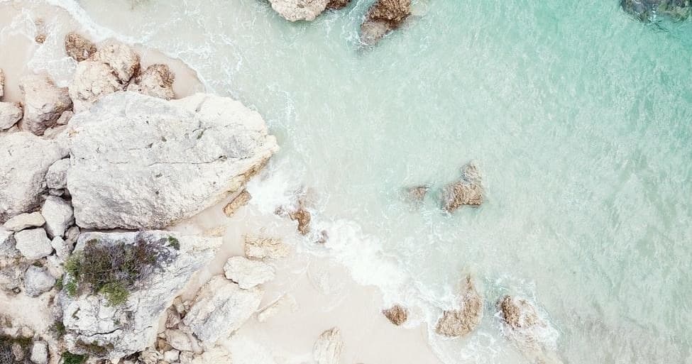 Aerial pale-rock beach with mint-green water and calm shoreline