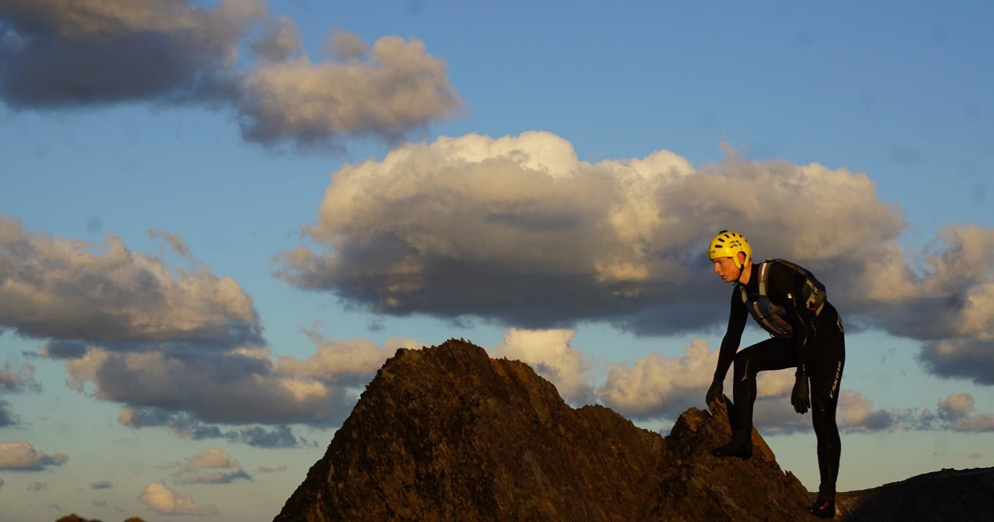 Rock climber ascending coastal sea stack under dramatic clouds