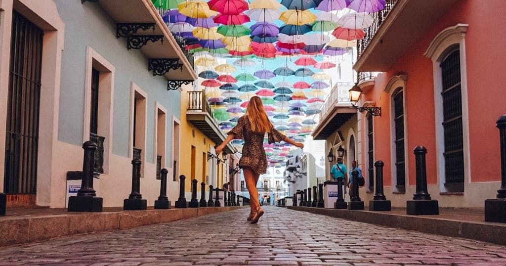 Woman walking under colorful umbrella canopy on cobblestone street