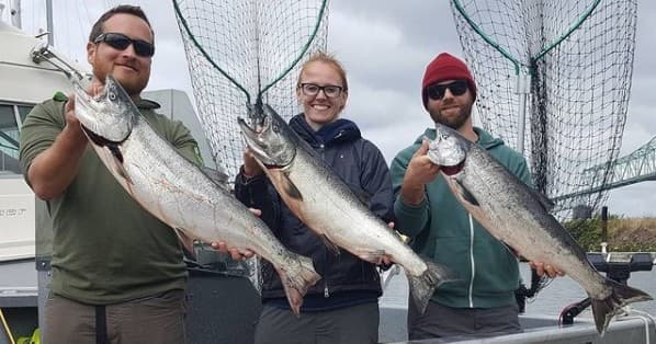 Three anglers holding caught salmon on charter boat by bridge