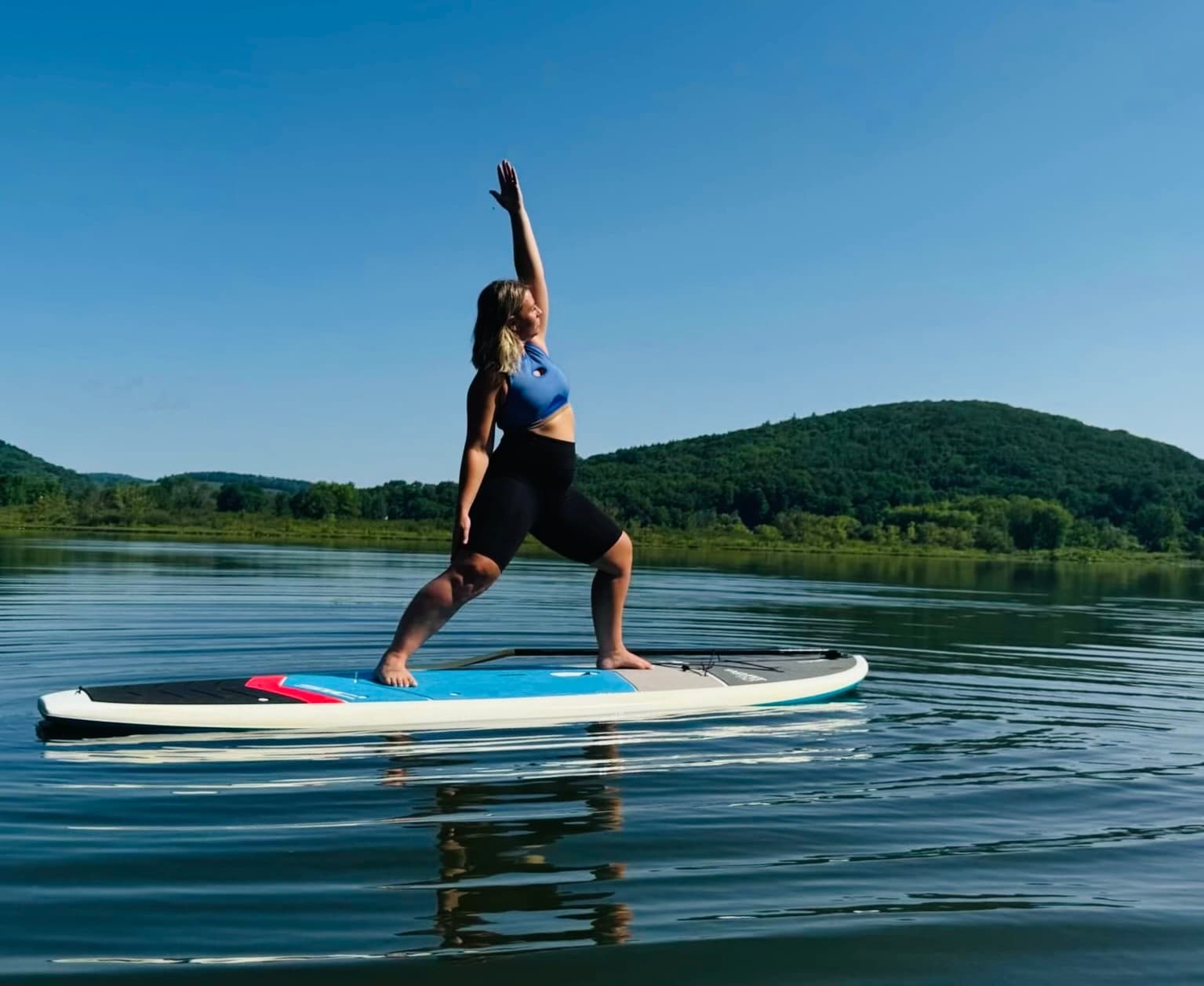 Person doing SUP yoga on calm lake with green hills background