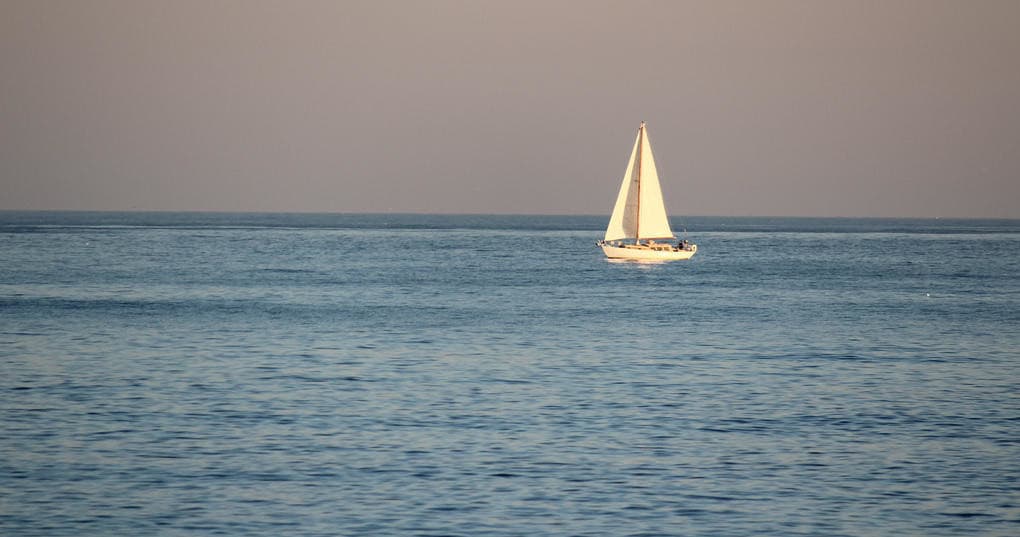 Single sailboat sailing on calm open ocean at golden hour