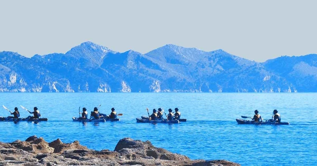 Sea kayakers paddling in calm Mediterranean bay with mountains