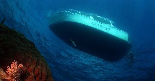 Scuba diving beneath boat hull near colorful coral reef