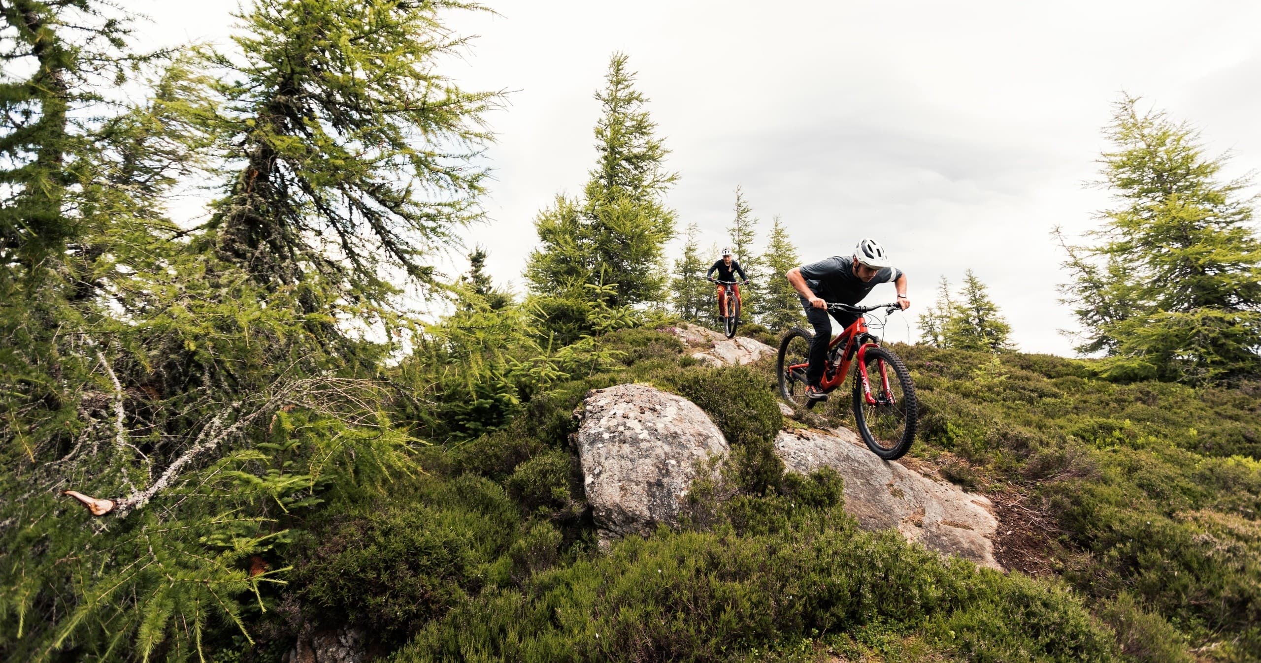 Mountain biker dropping over rocky ridge in forested highlands