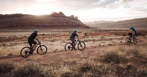 Mountain bikers riding sunset desert trails in canyon landscape