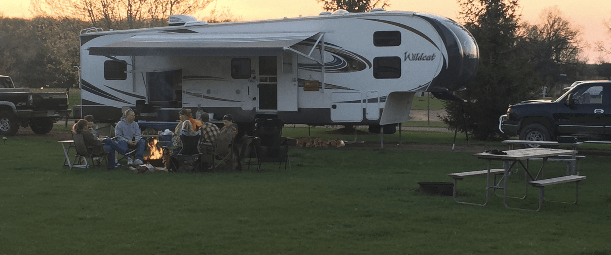 RV camping with campfire on grassy lakeside campsite at sunset