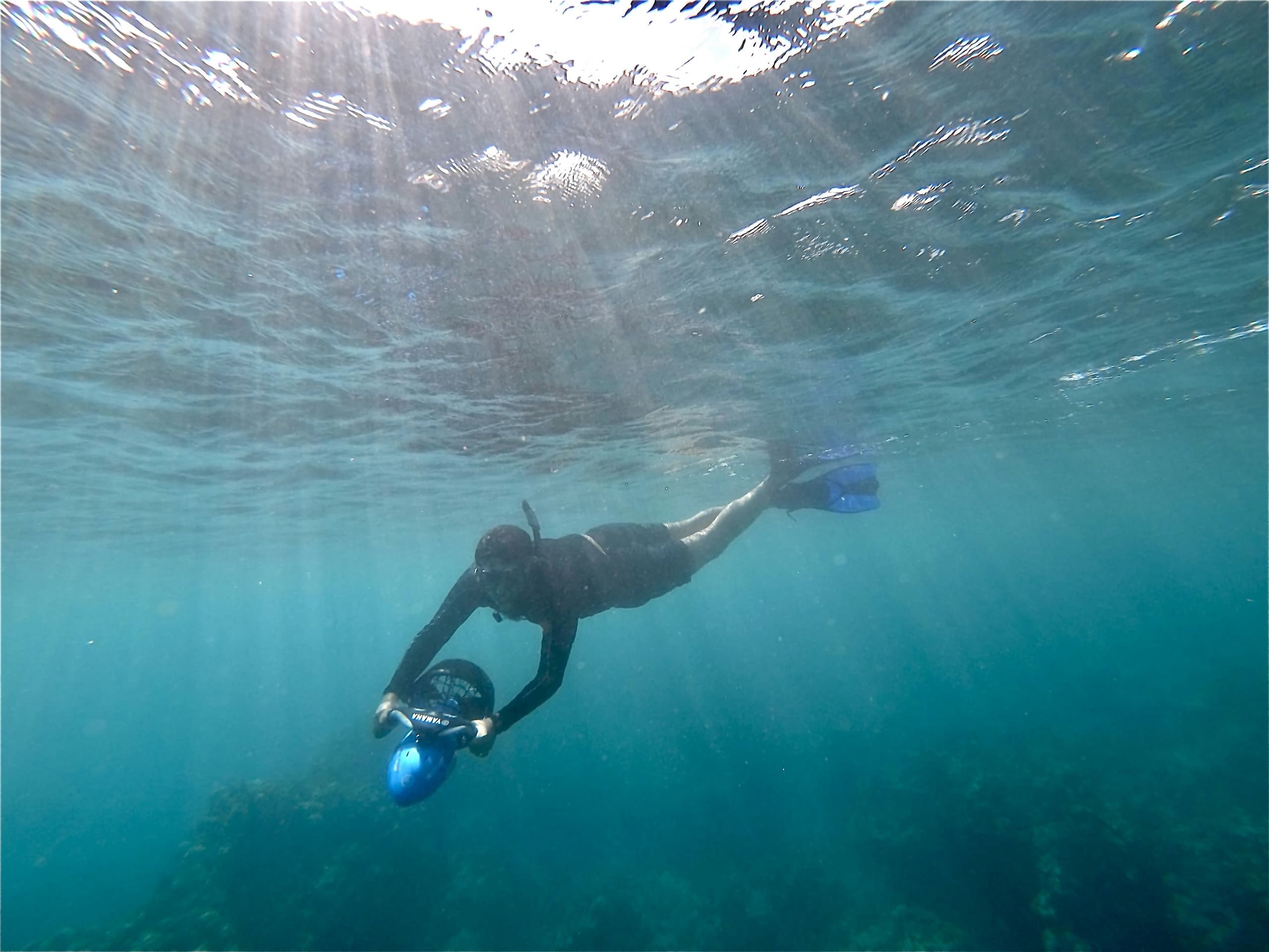Snorkeler with sea scooter underwater over coral reef, crystal water