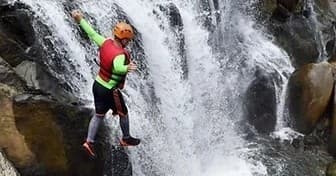 Canyoneer jumping beside a steep tropical waterfall, canyoning action