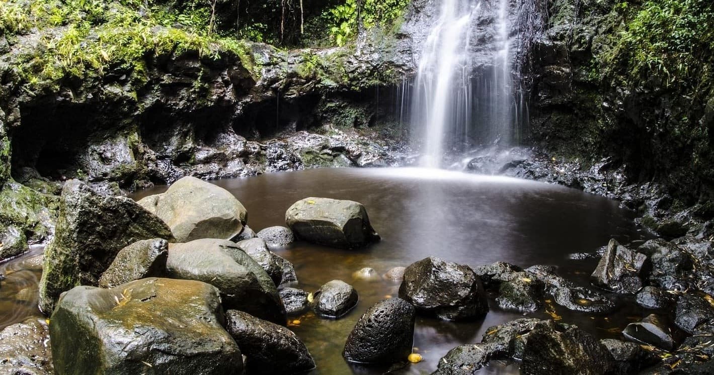 Waterfall cascading over rocks in lush Hawaiian rainforest pool