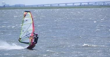 Windsurfer cutting through choppy coastal waters near bridge