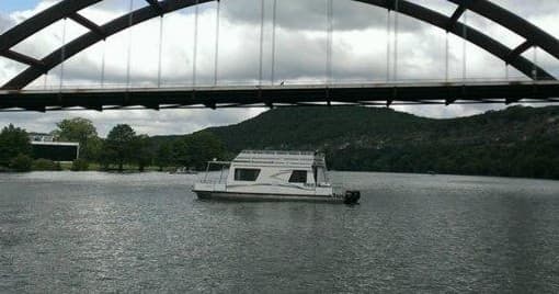 Houseboat cruising under arched bridge on Lake Travis waters