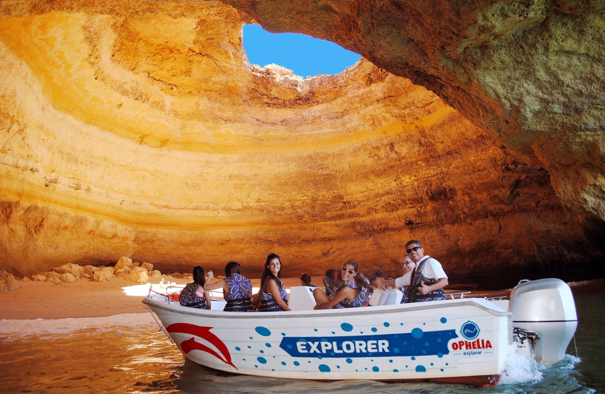 Small boat exploring golden sea cave interior in Algarve