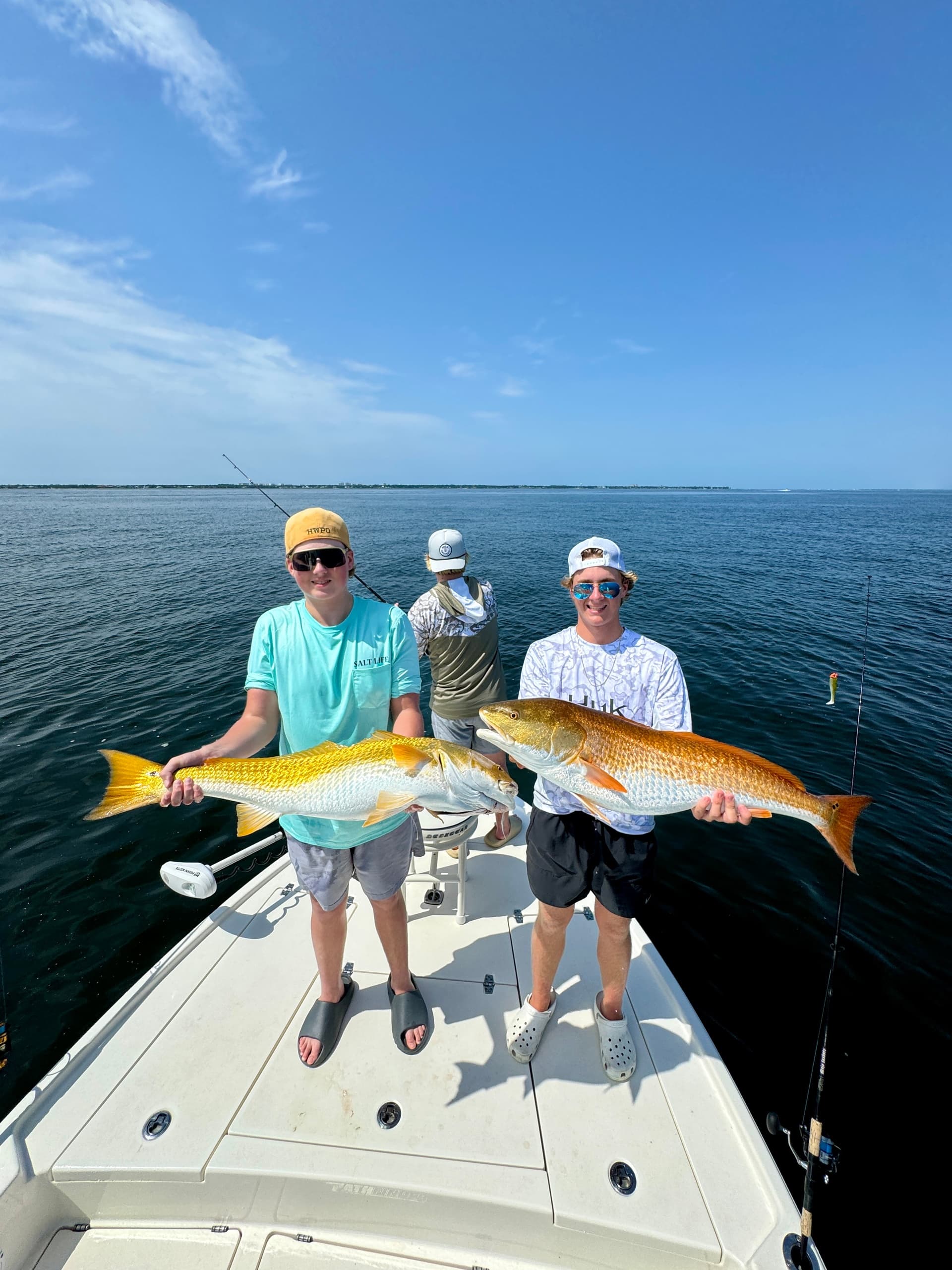 Three anglers displaying redfish on boat bow in calm bay