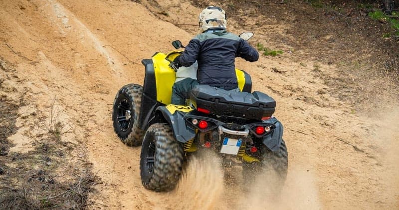 Rider on yellow ATV climbing sandy hill in desert terrain