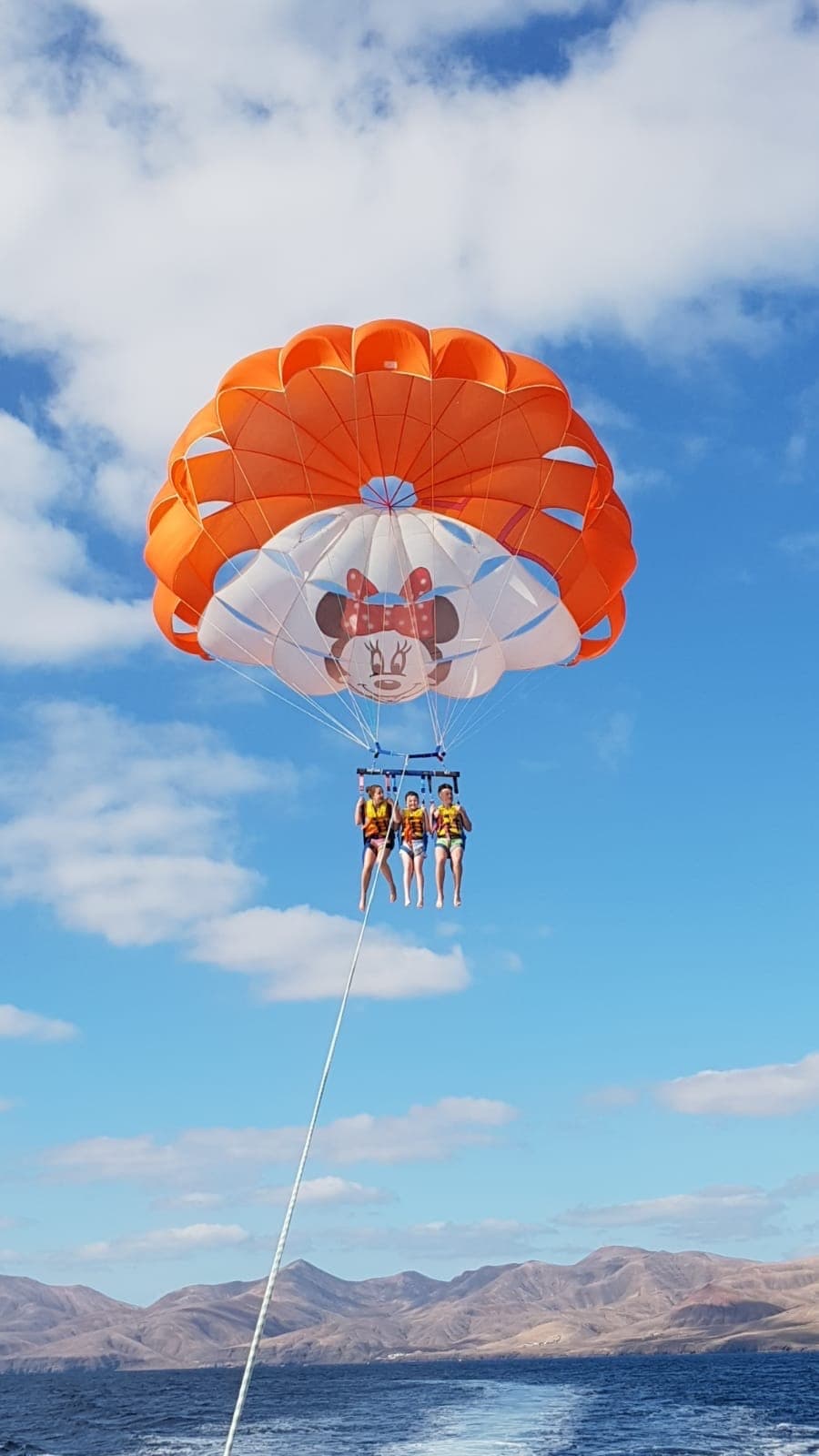 Dual parasailers ascending over blue sea with mountains
