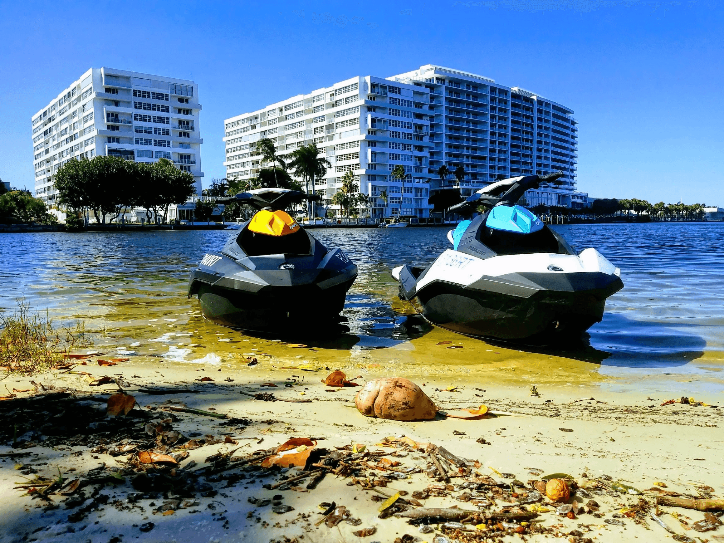 Two rental jet skis beached on sandy bay near waterfront condos