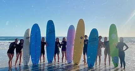 Group of surfers with colorful boards on sunny beach shore