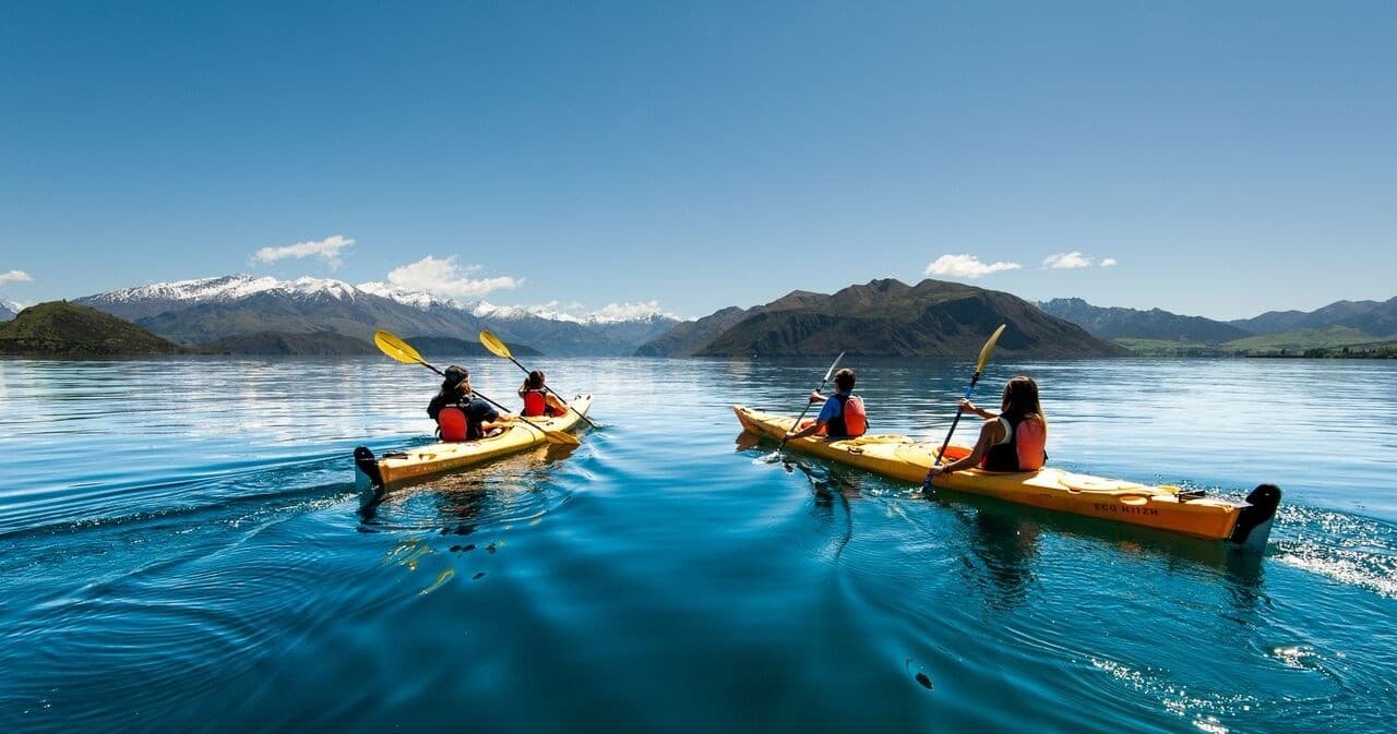 Kayakers paddling across clear alpine lake with mountain vistas