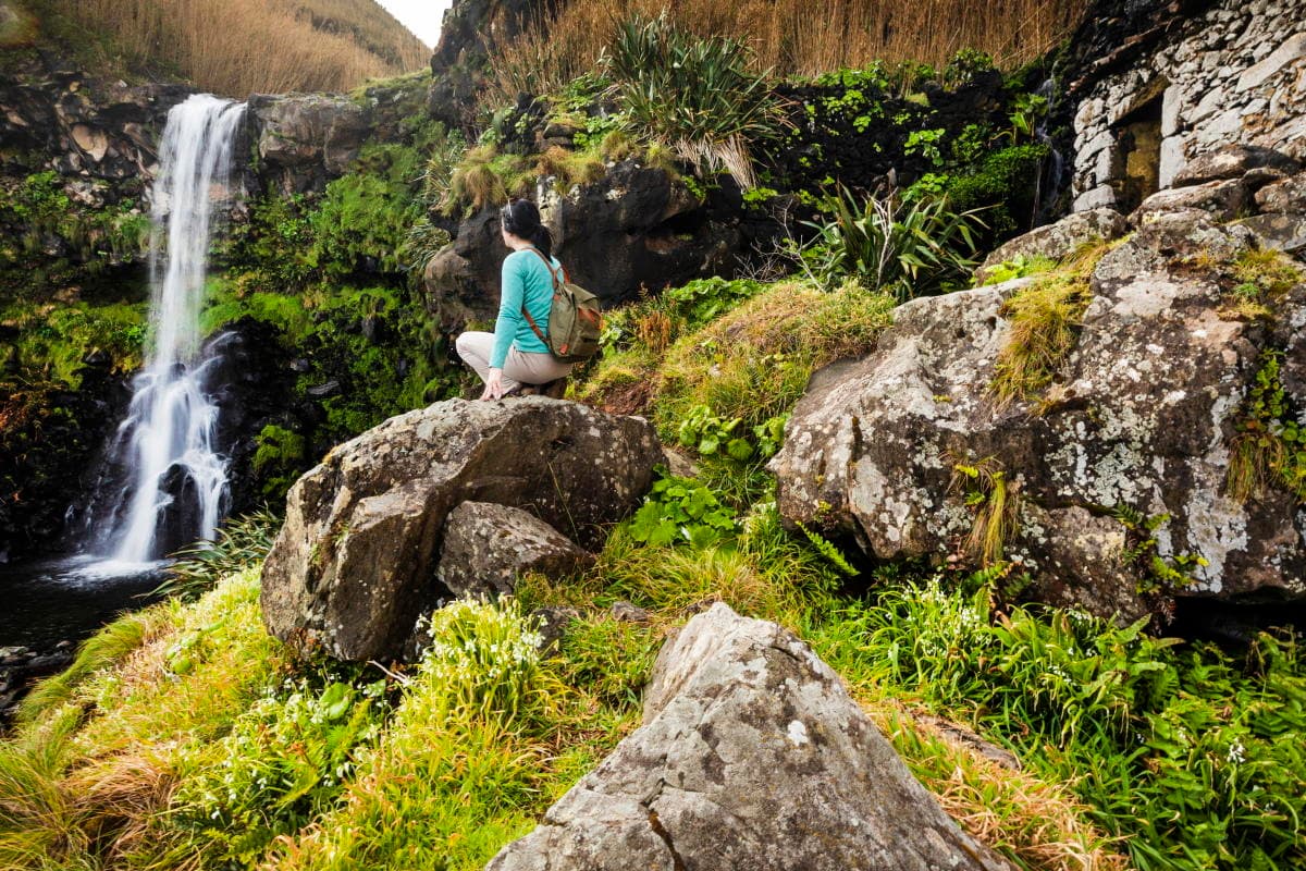 Hiker seated beside a small Azores waterfall amid green rocks