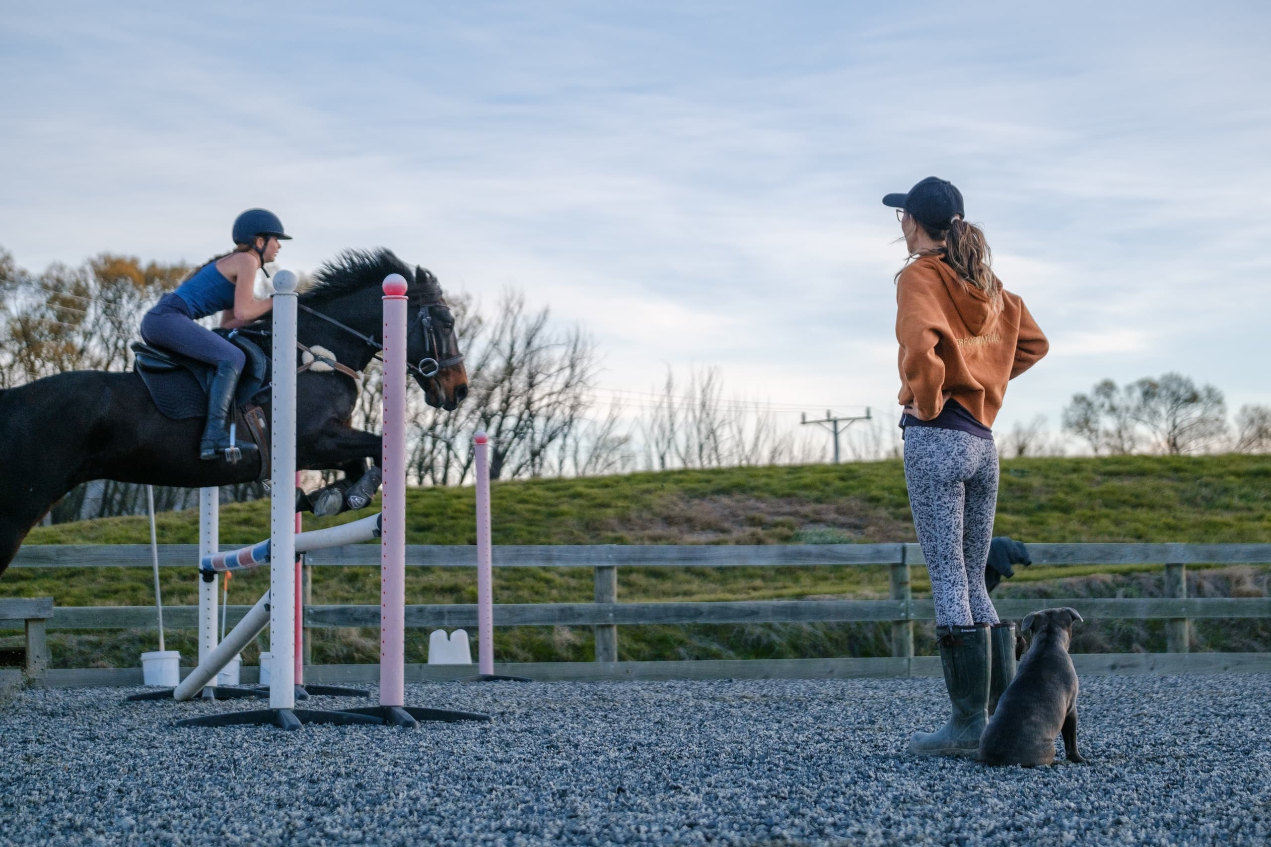 Show jumper clearing fence with trainer watching in outdoor arena