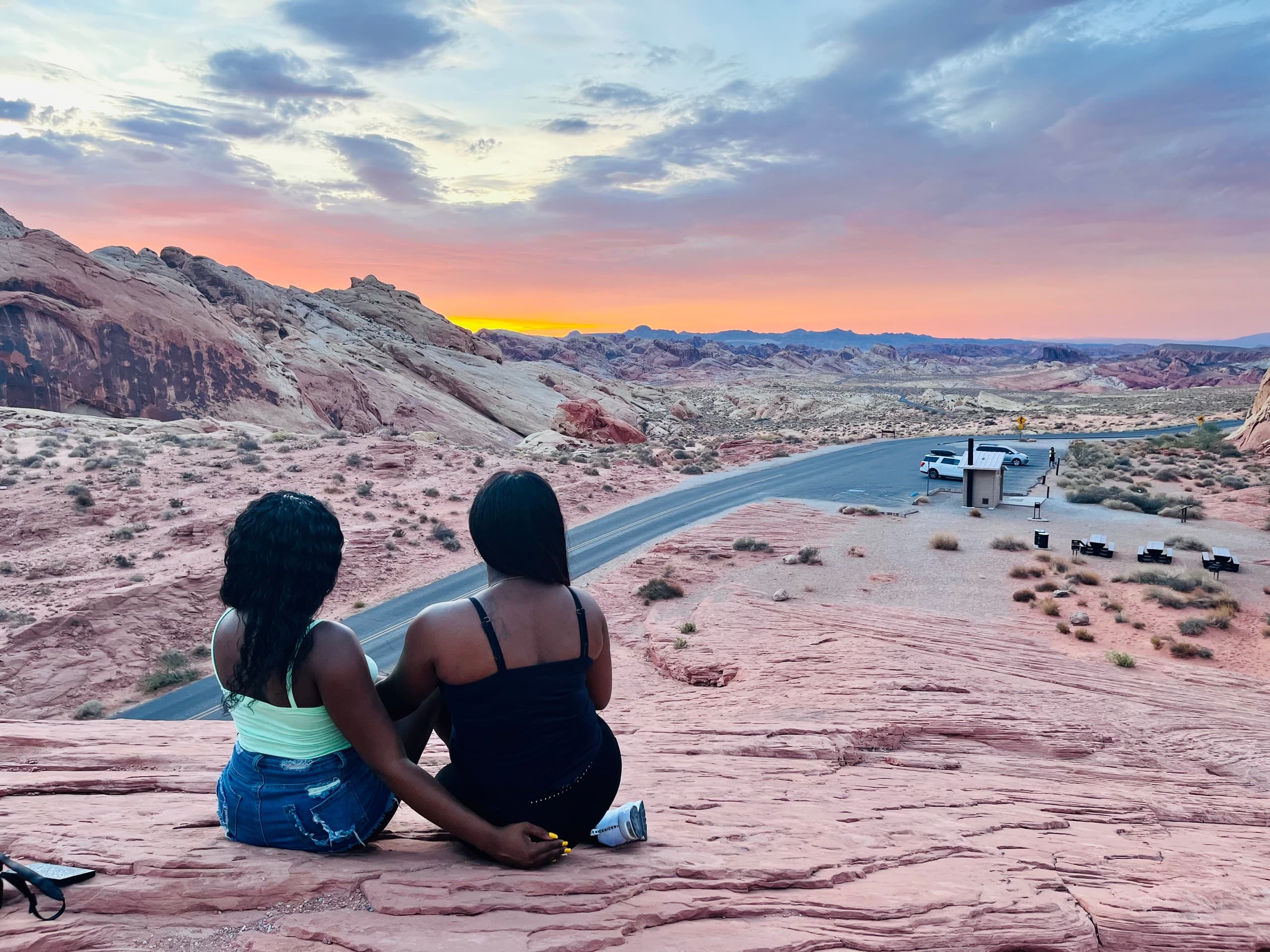 Two women sitting on desert overlook watching sunset over canyon