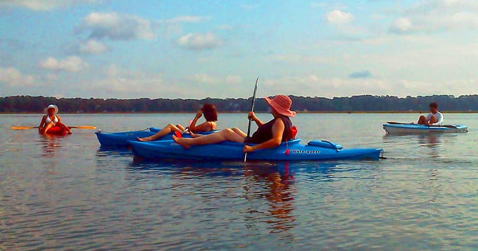 Group of kayakers reclining on flat kayaks in calm estuary waters