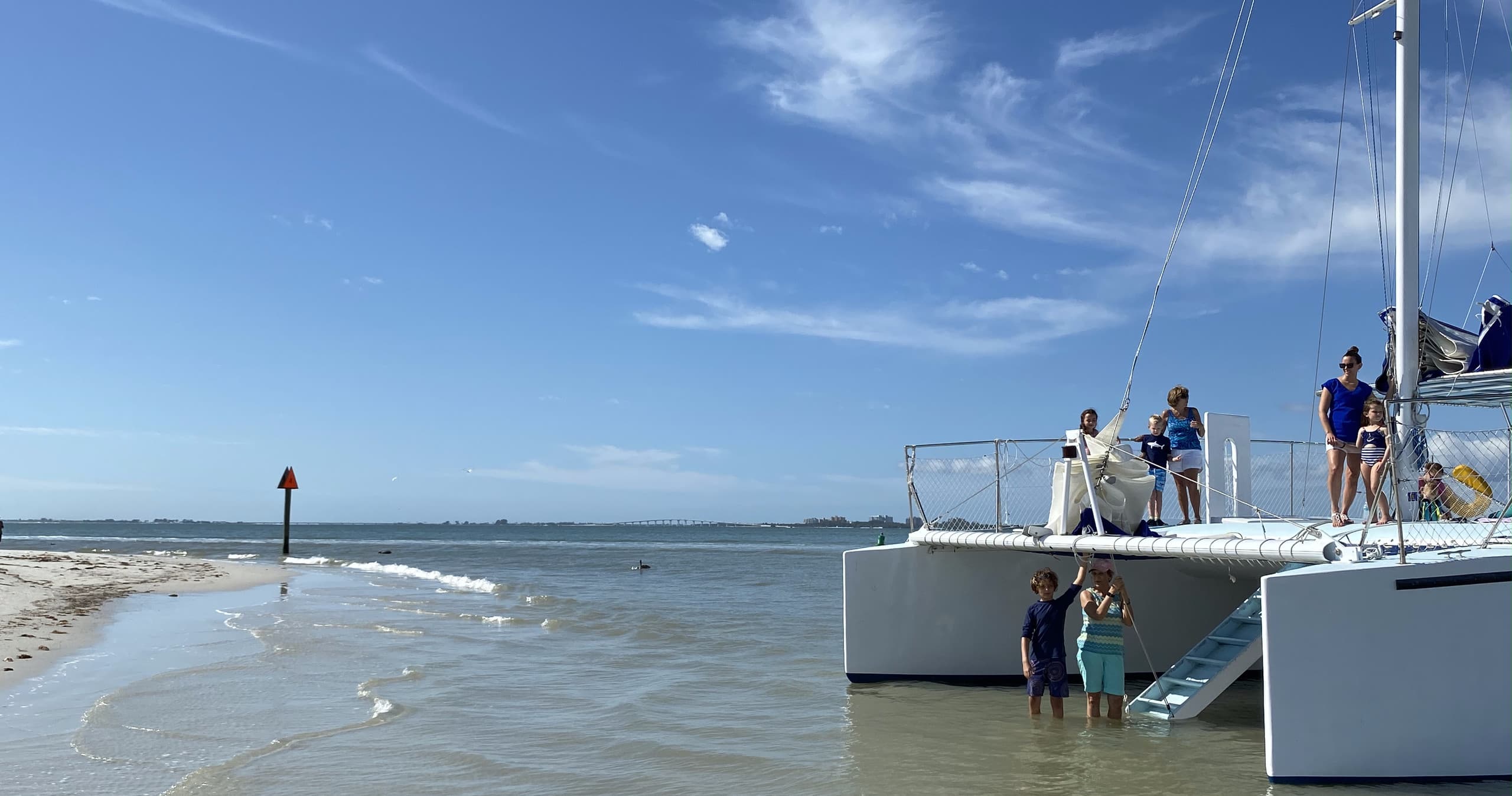 Catamaran anchored near sandy shore with guests boarding