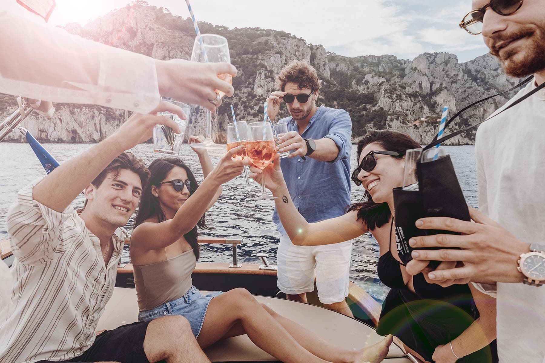 Group toasting drinks on yacht near rocky coastal cliffs at sunset