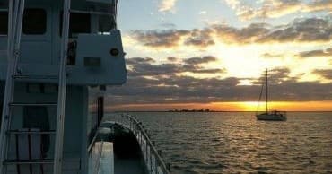 Sunset view from boat with calm horizon and moored sailboat