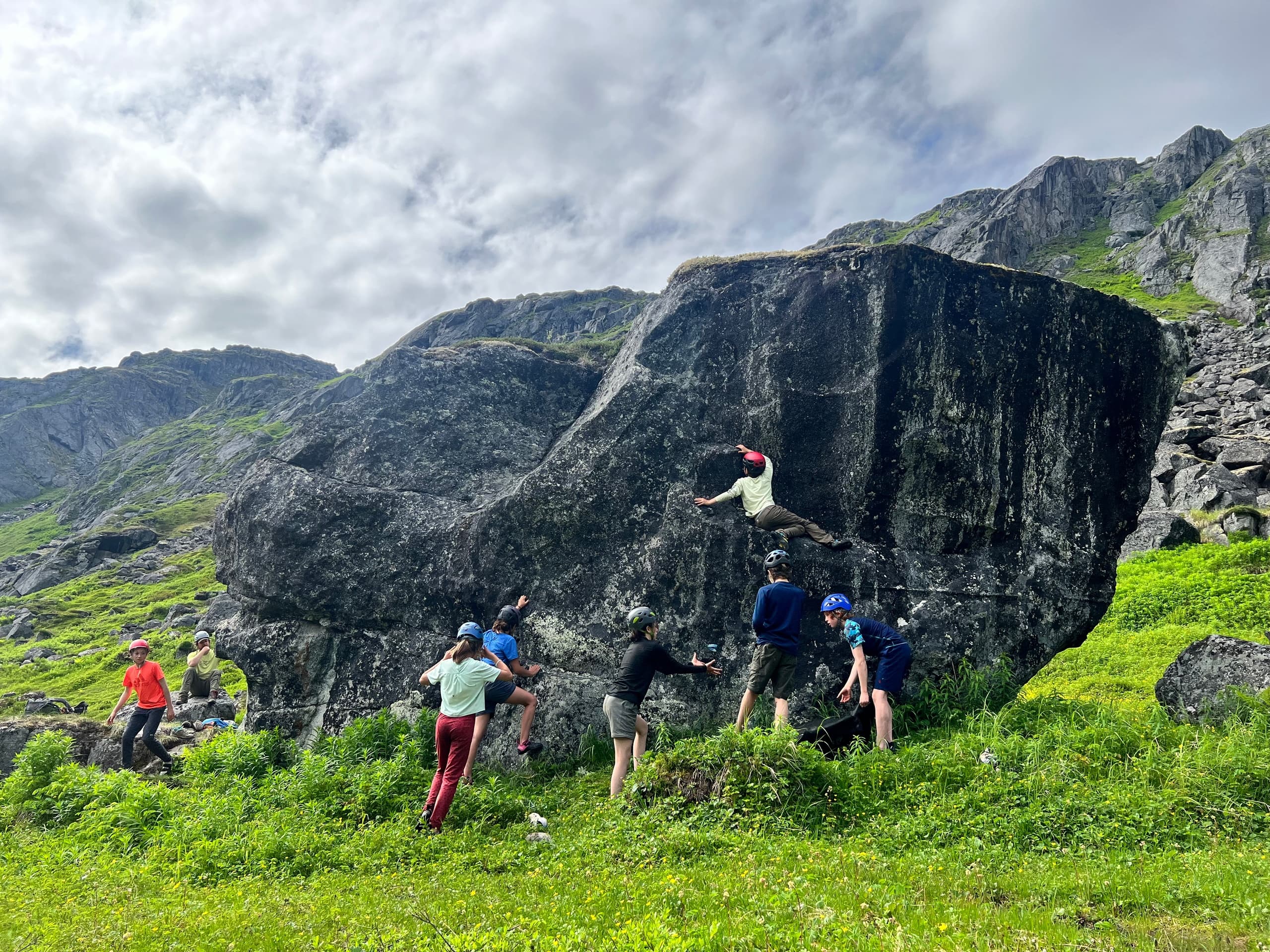 Group hiking through green mountain meadows with rocky cliffs