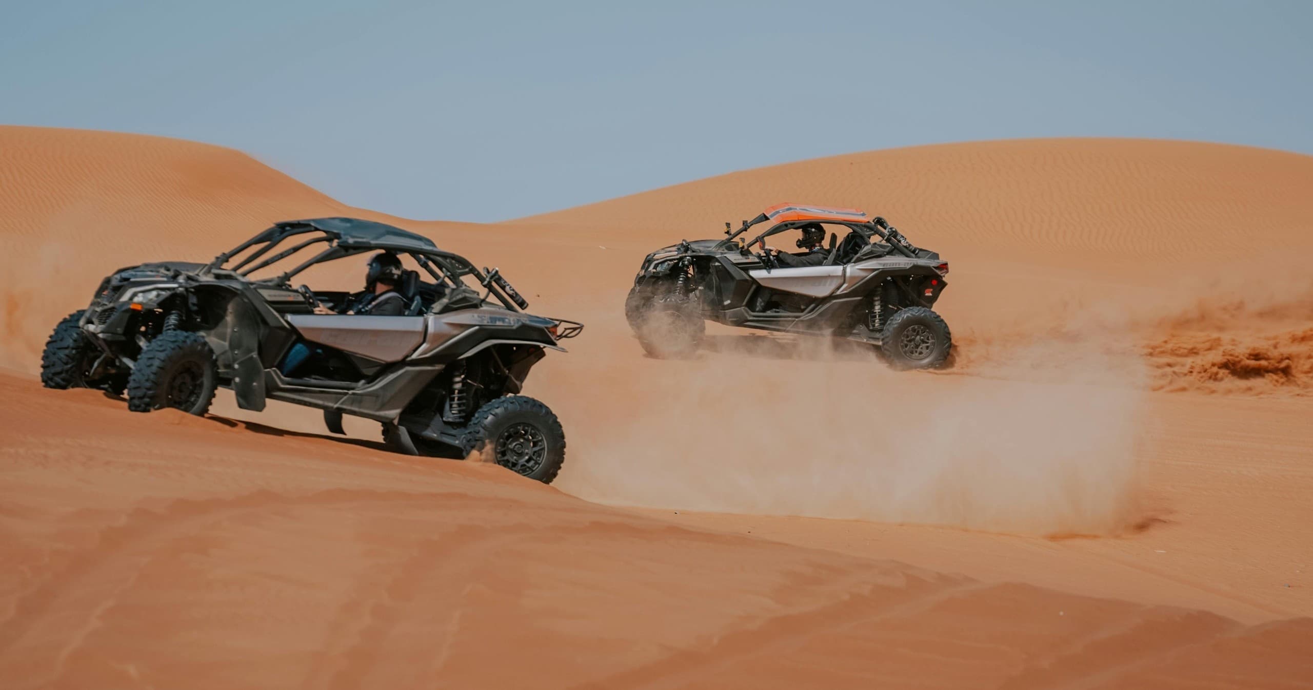 Two UTVs kicking sand on desert trail, high-speed off-road action