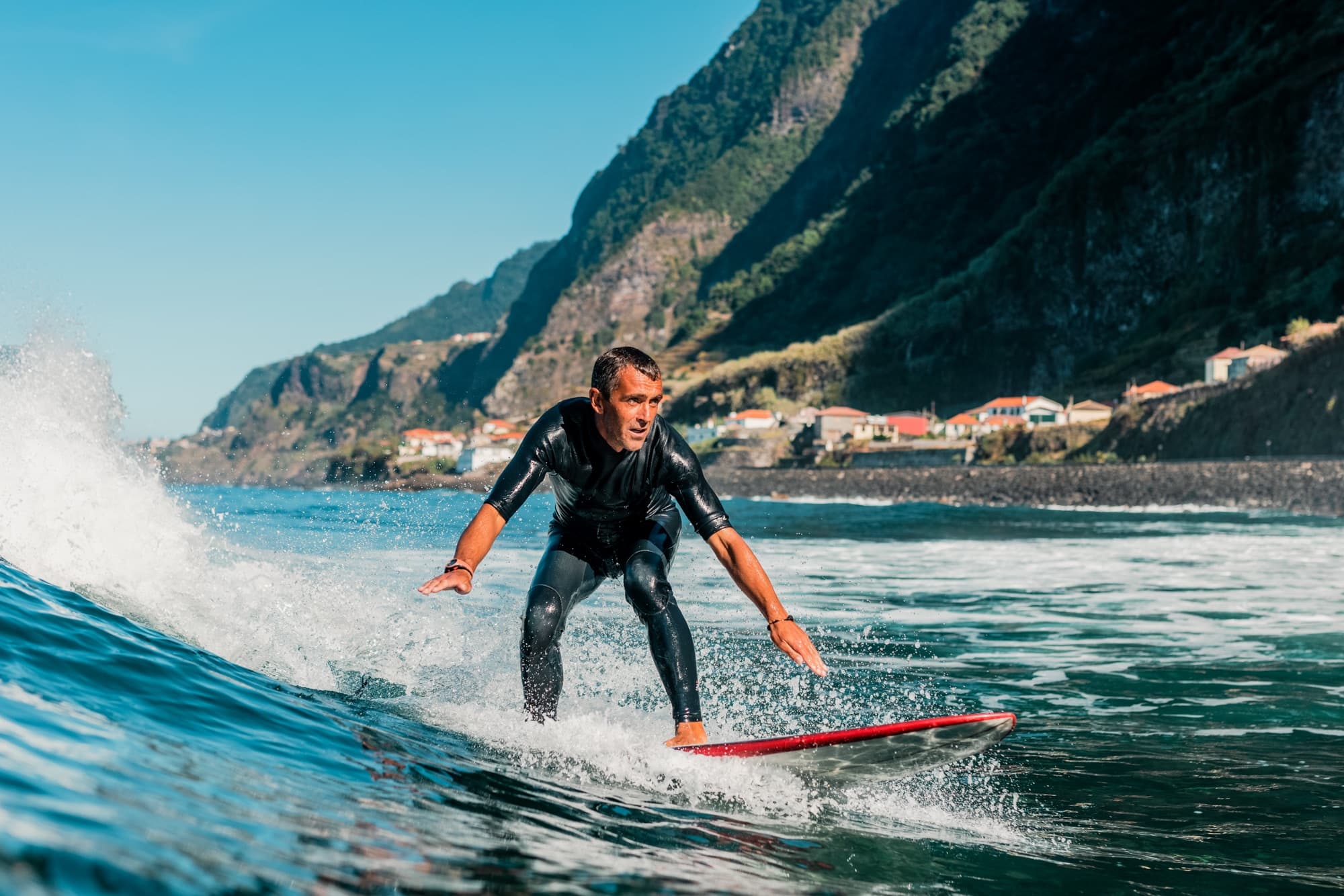 Surfer riding near mountain shoreline with sunny coastal backdrop