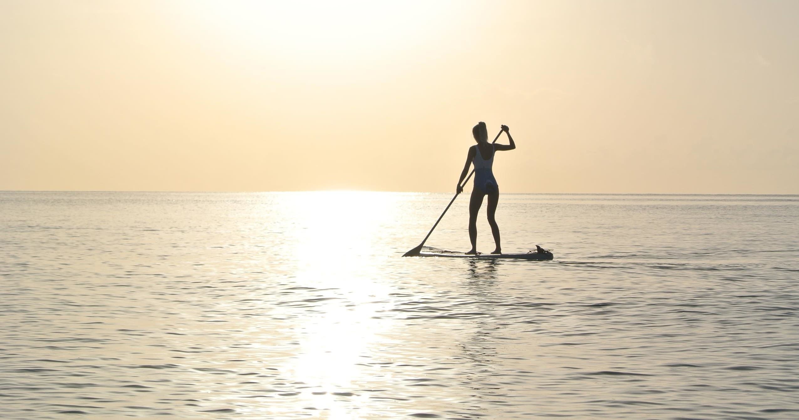 Stand-up paddleboarder silhouetted at sunset on calm open ocean horizon