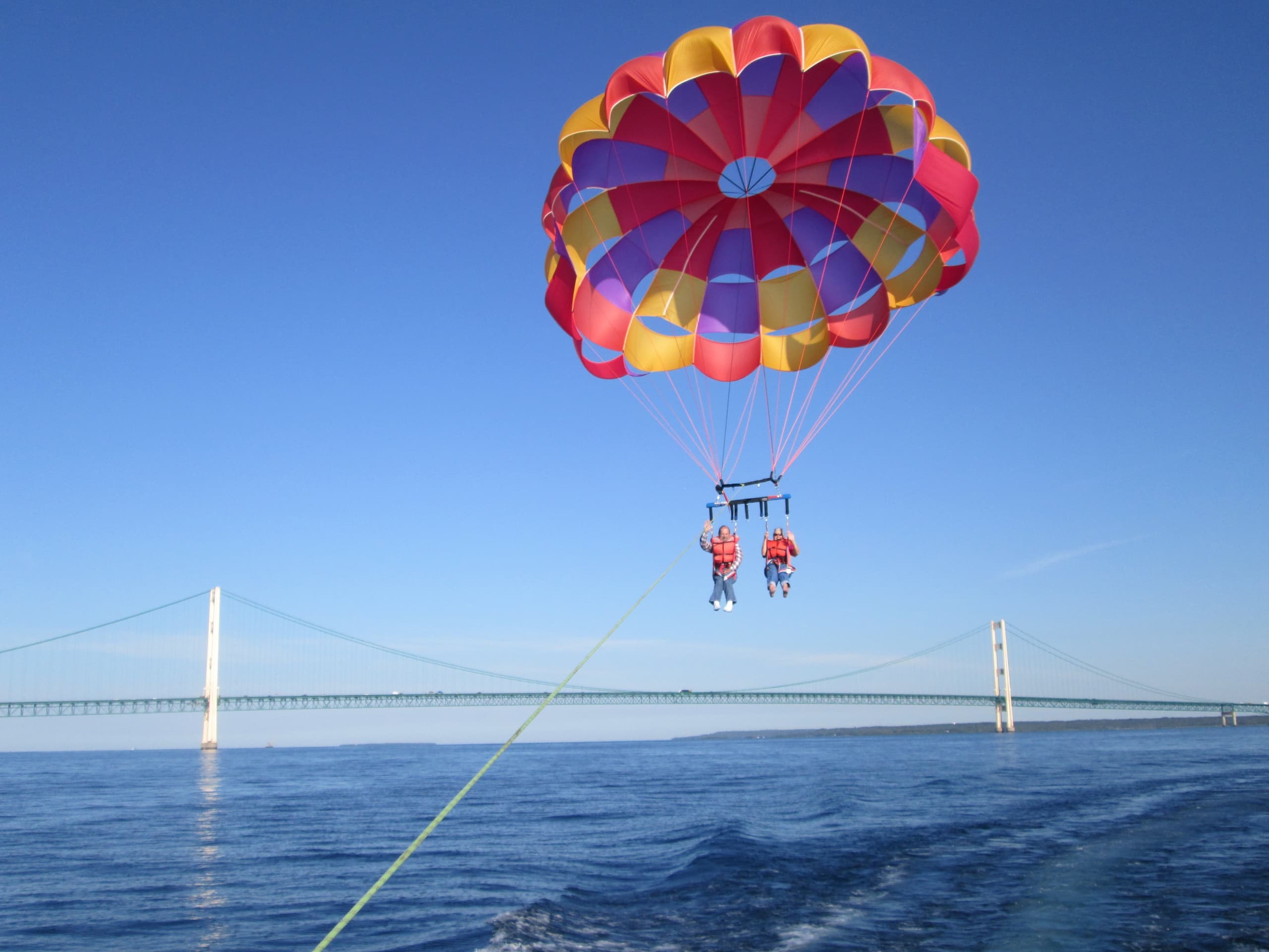 Tandem parasailing over open water with bridge backdrop