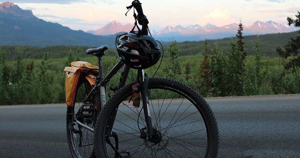 Touring bike silhouetted at sunset with alpine ridgeline