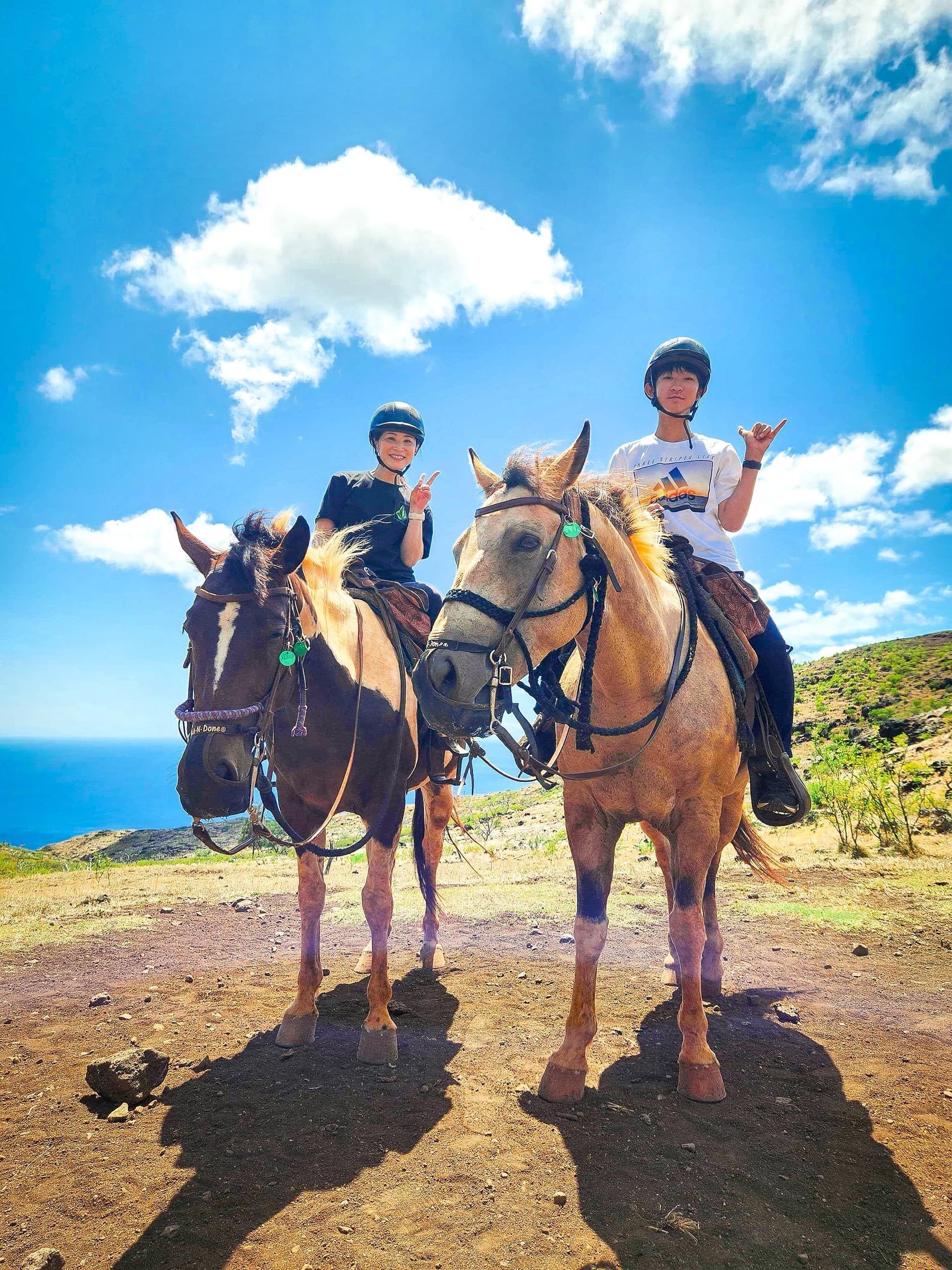 Two riders horseback riding on coastal trail with ocean backdrop