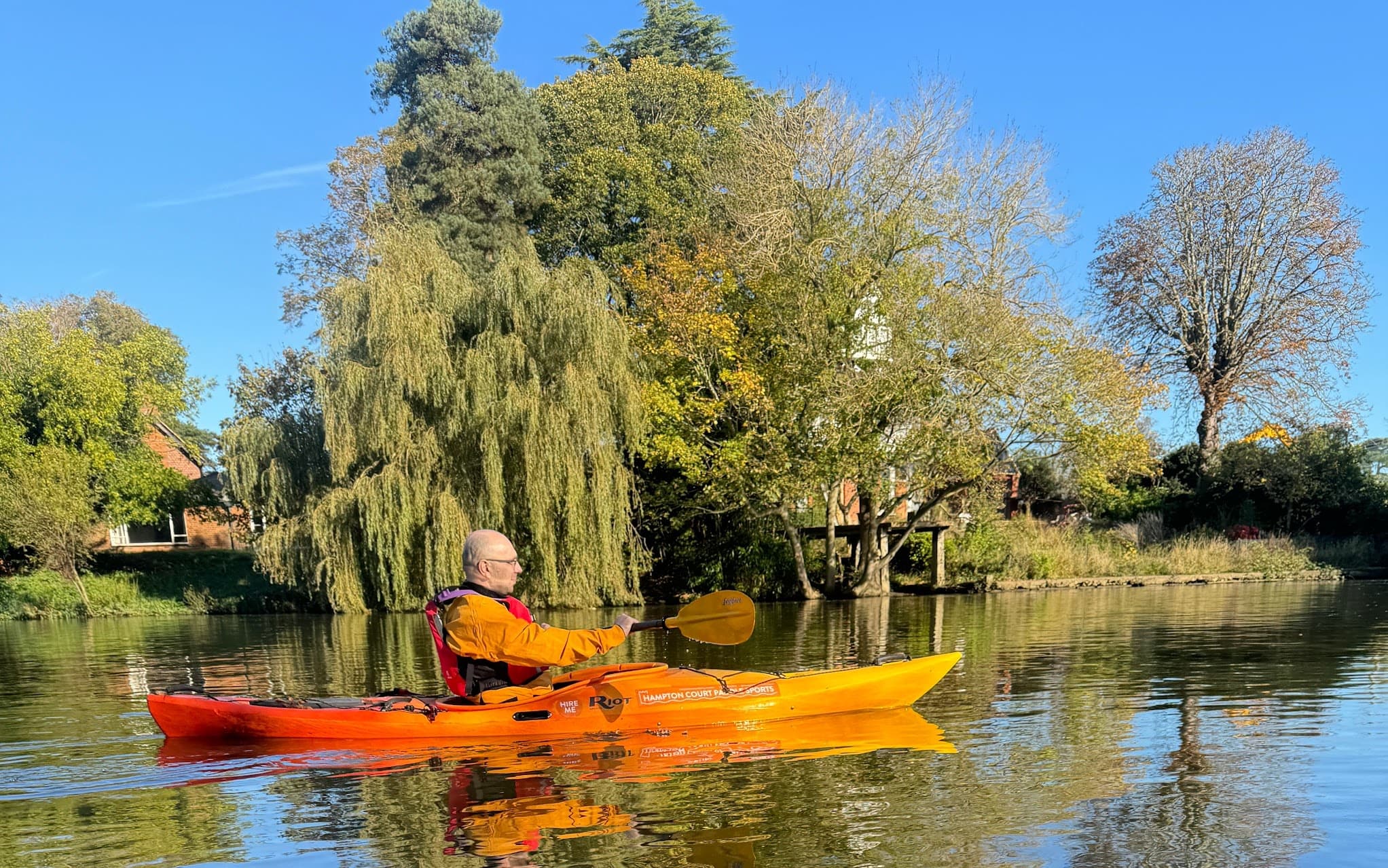 Solo kayaker paddling past willow trees on tranquil river