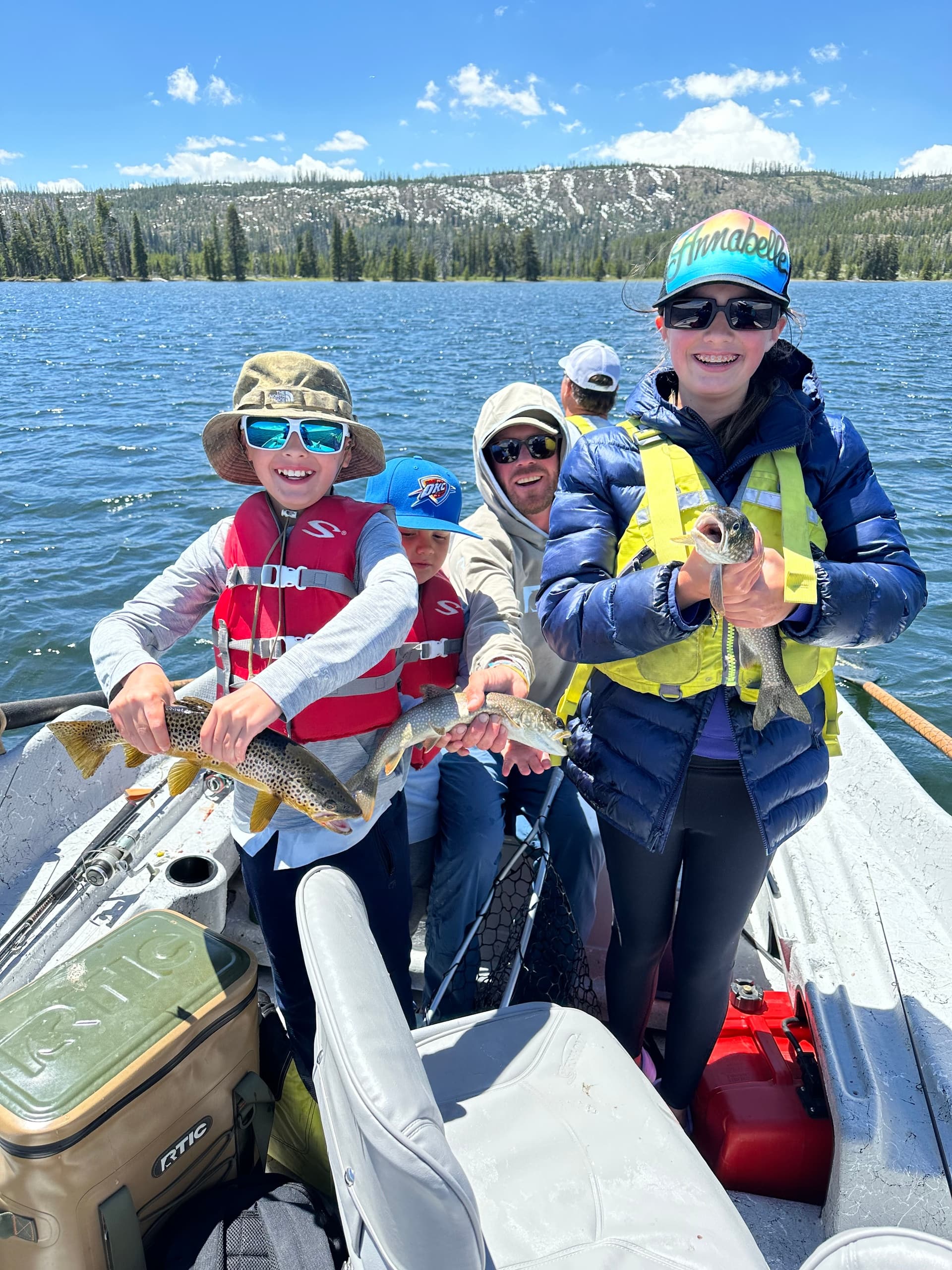 Family anglers holding freshwater trout on mountain lake boat