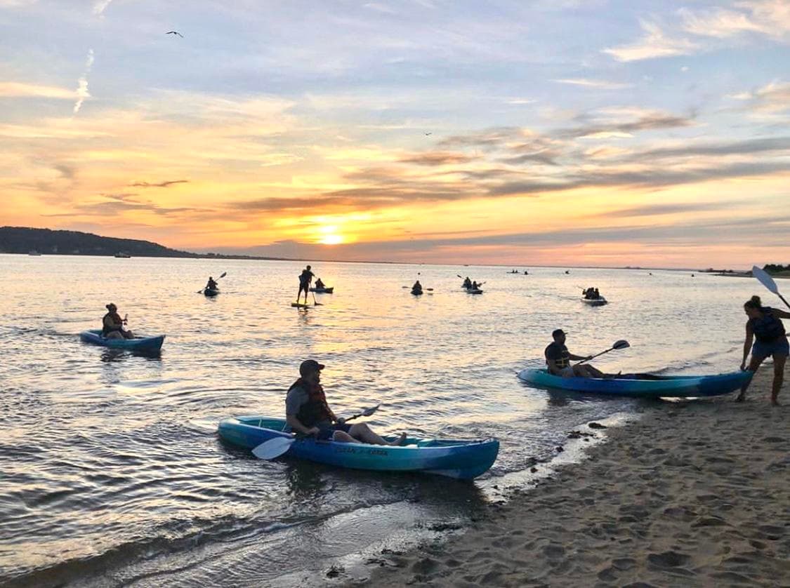 Kayakers launching from beach into colorful sunset over bay