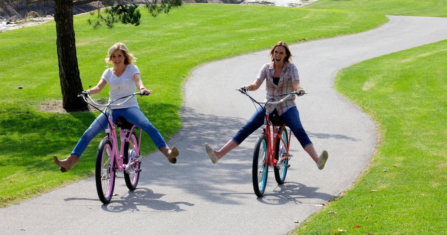 Two friends riding bikes playfully along a paved park path